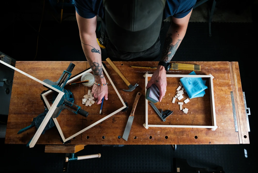 An overhead view of a craftsperson assembling wooden frames on a workbench.