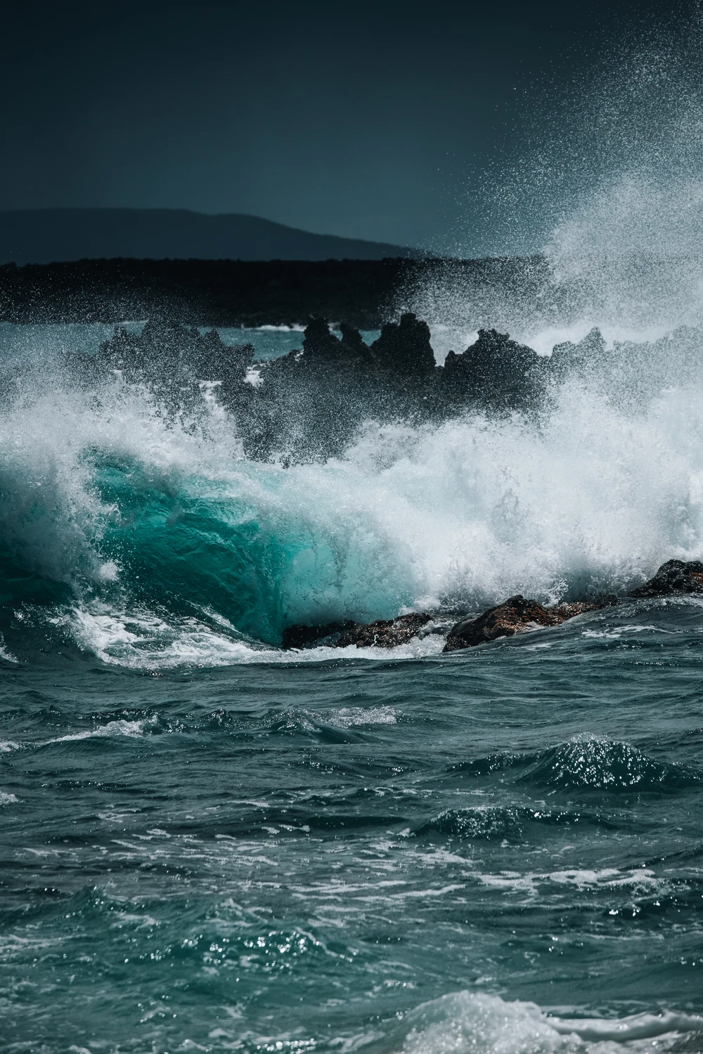 A turquoise wave breaking against dark rocks.