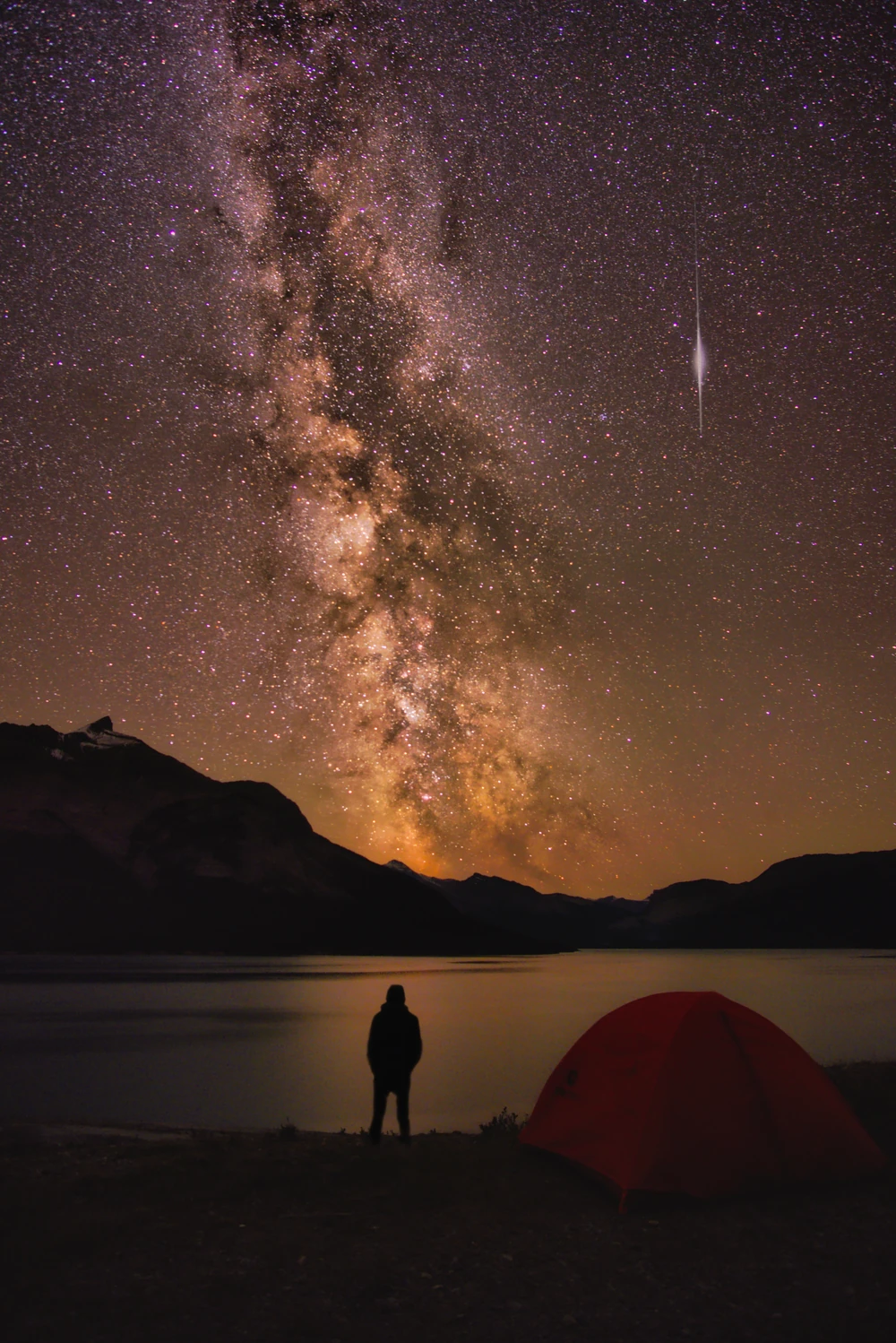 A self portrait of myself and tent beside a lake under the milky way in Abraham lake