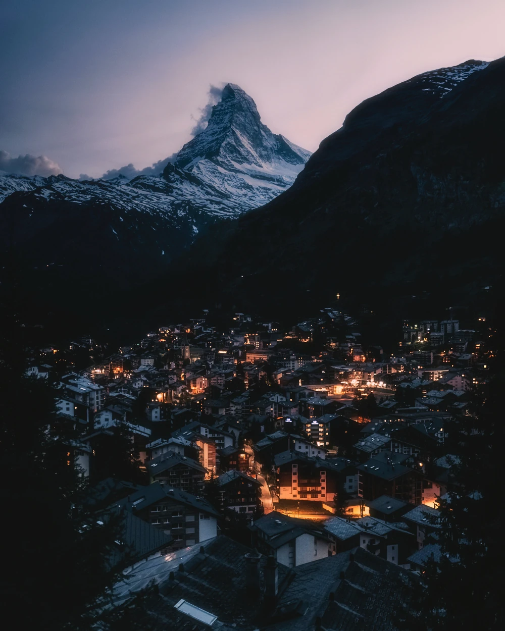 Warm lights in an alpine village beneath a mountain at dusk.
