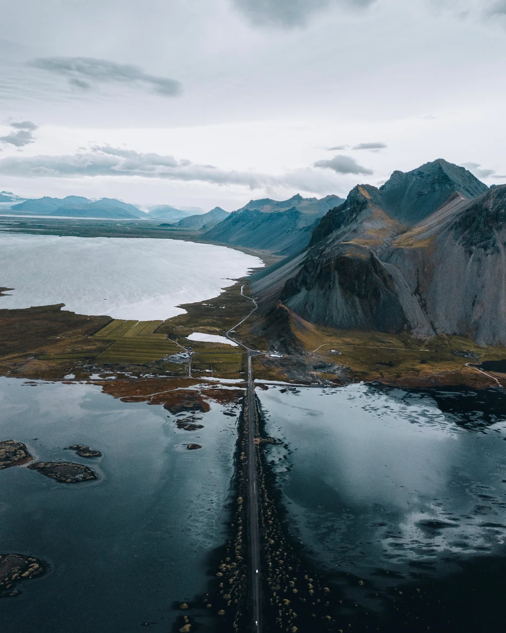 A straight road between the ocean and rugged coastal mountains.