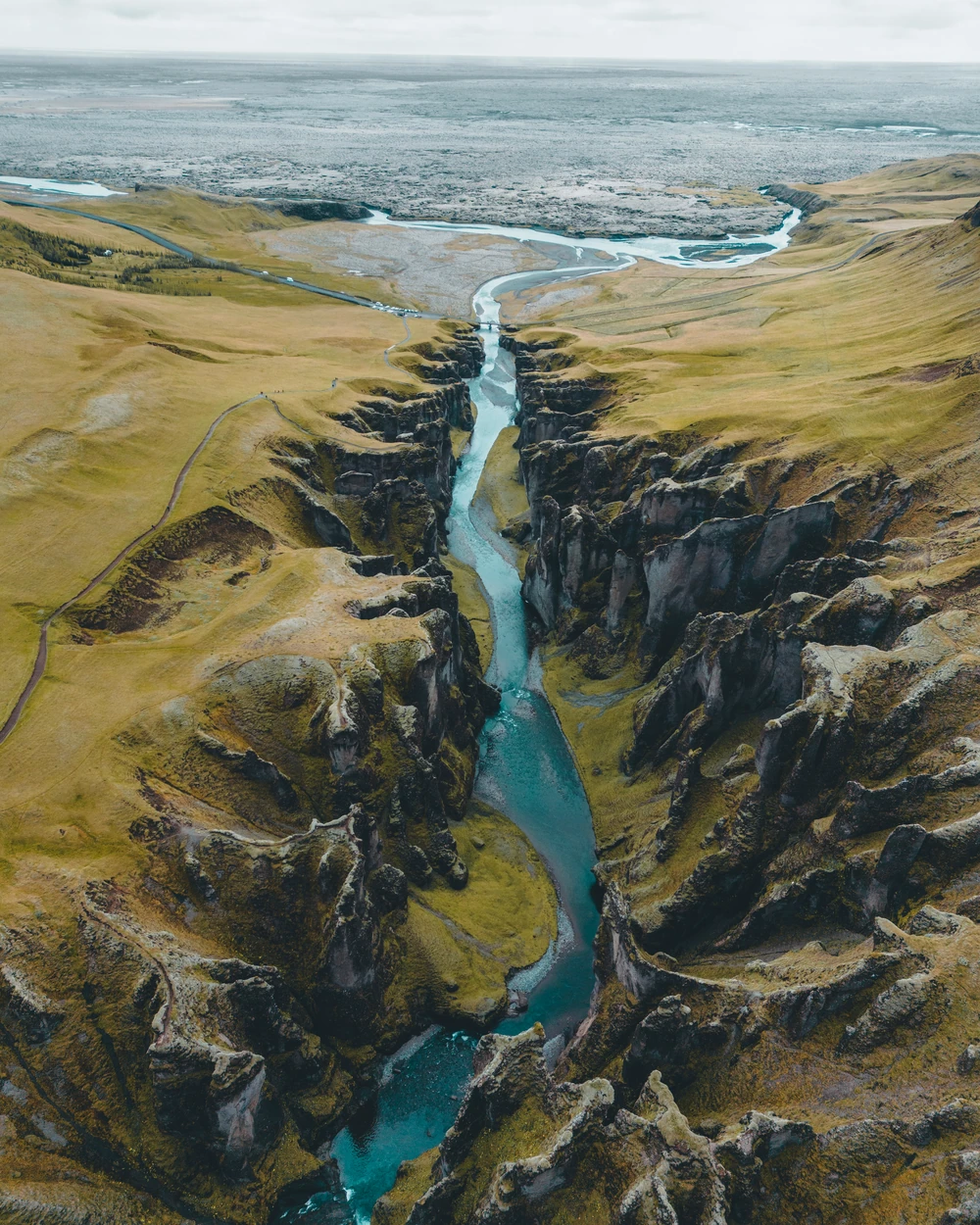 A turquoise river winding through a green and dark rock canyon, seen from above.
