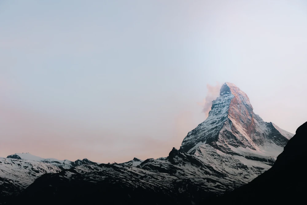 A snow-covered pointed Matterhorn against a soft pink and pale blue sky.