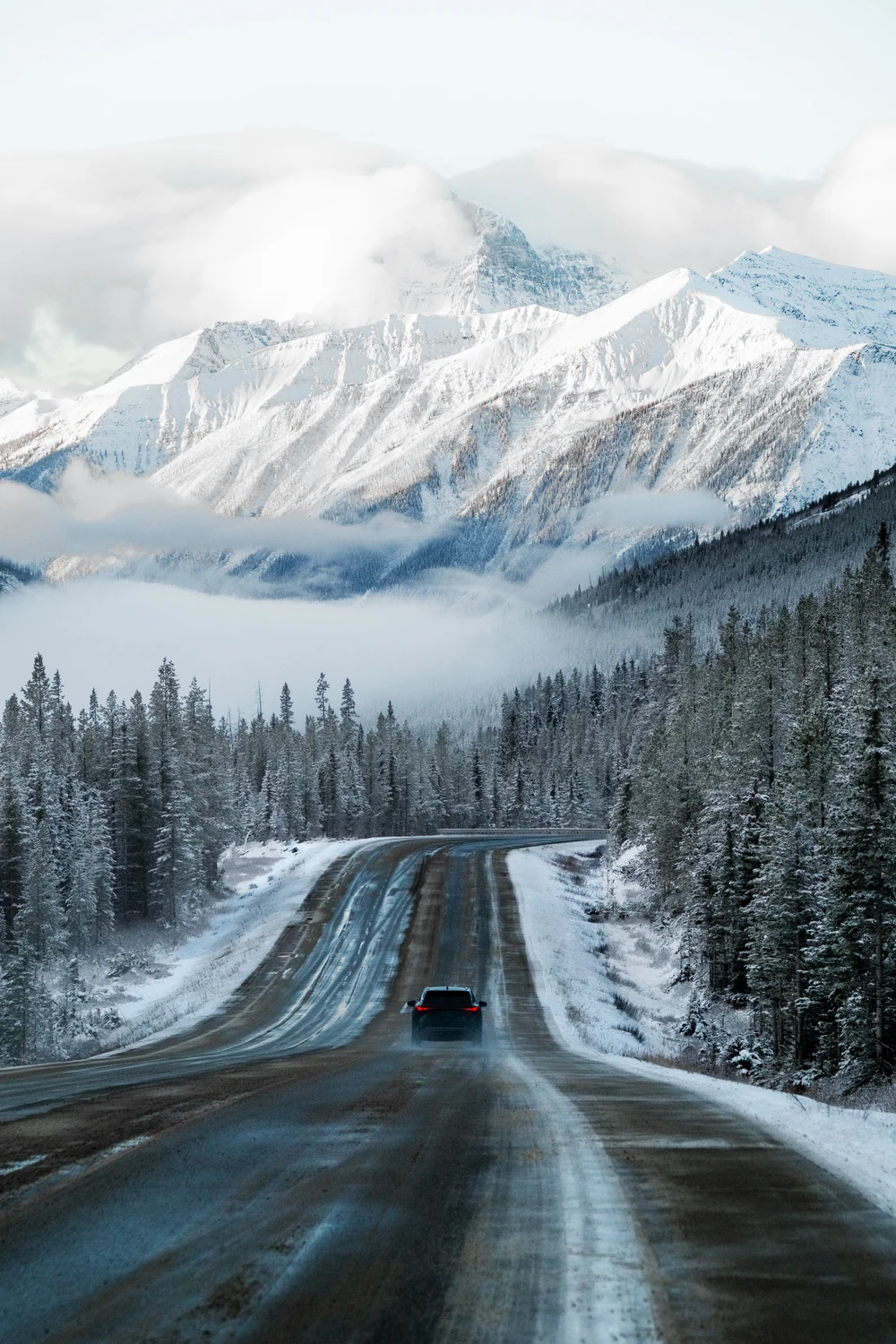 A small vehicle travelling along a winter road toward snow-covered mountains.