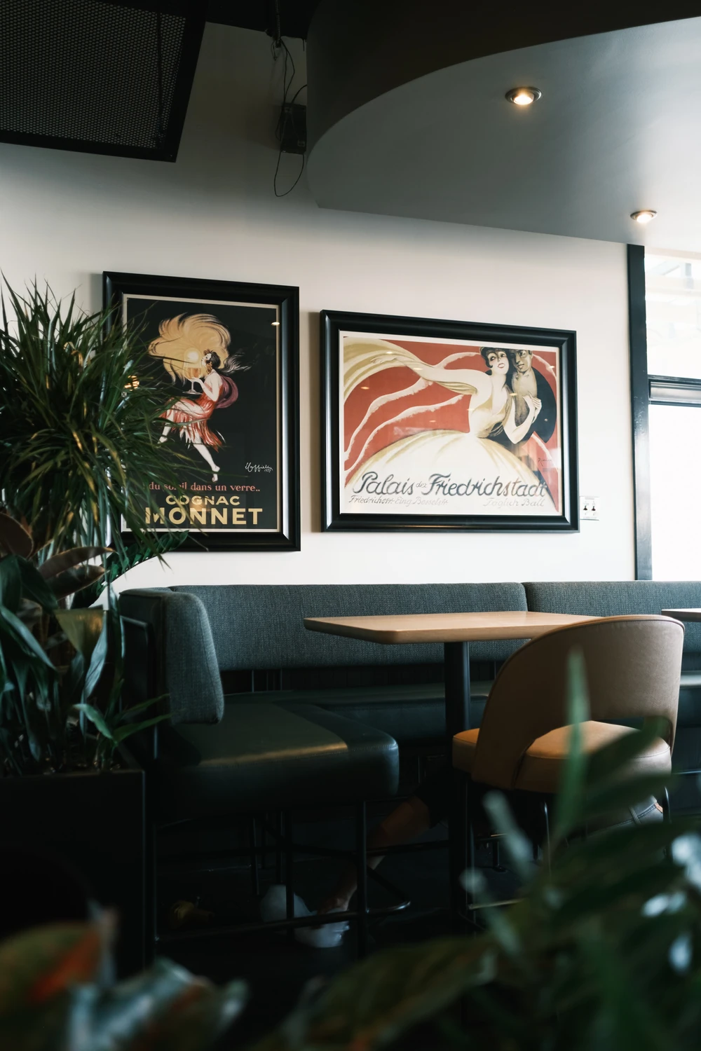 Two framed vintage posters above a grey upholstered booth at Earls, with plants and warm wood furniture.