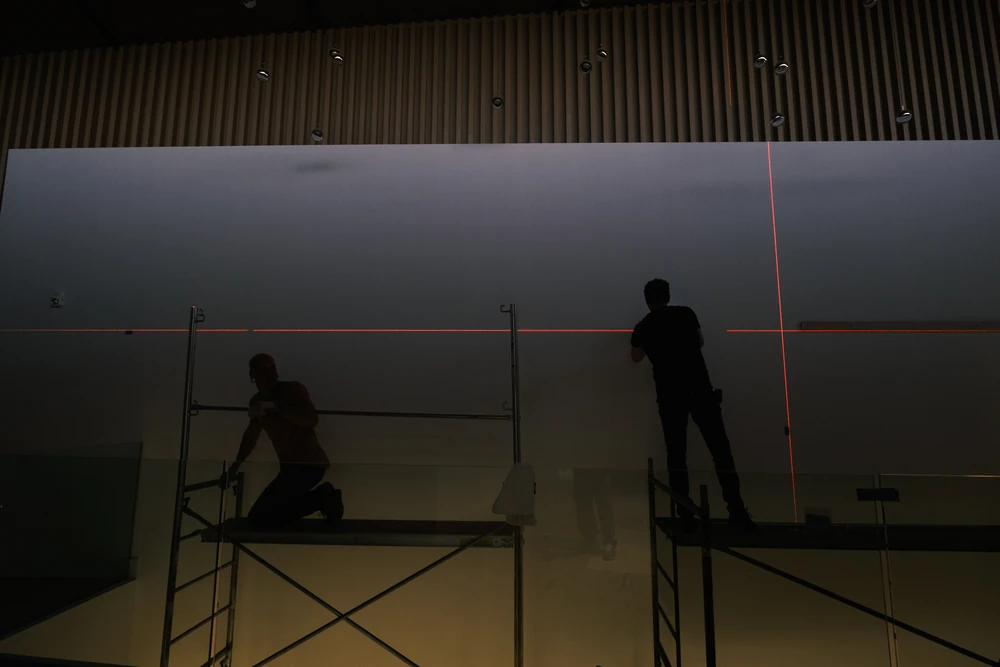 Silhouetted installers working with laser alignment lines in a dark interior.