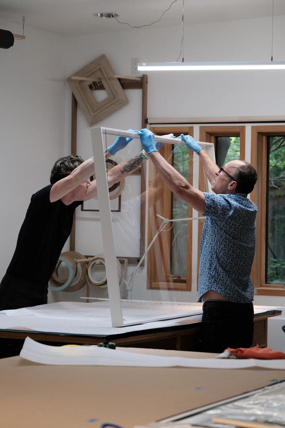 Two workers lifting a large frame in the workshop.