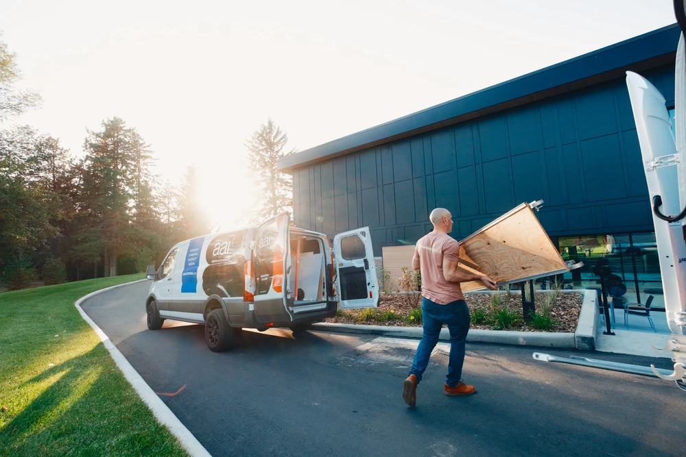 An installer arriving with artwork beside vehicles in warm, low light.