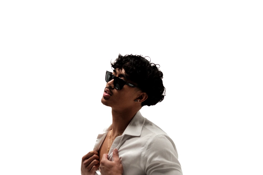 An artist in a white shirt and dark glasses against a bright white backdrop.