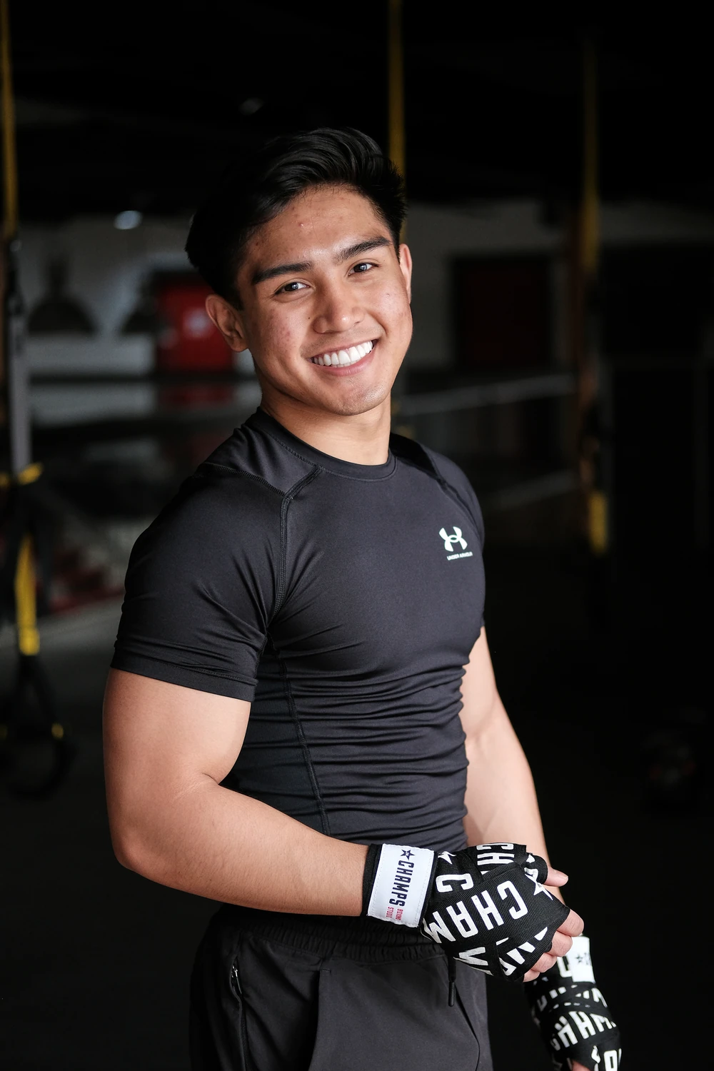 A smiling athlete holding boxing gloves in a gym.