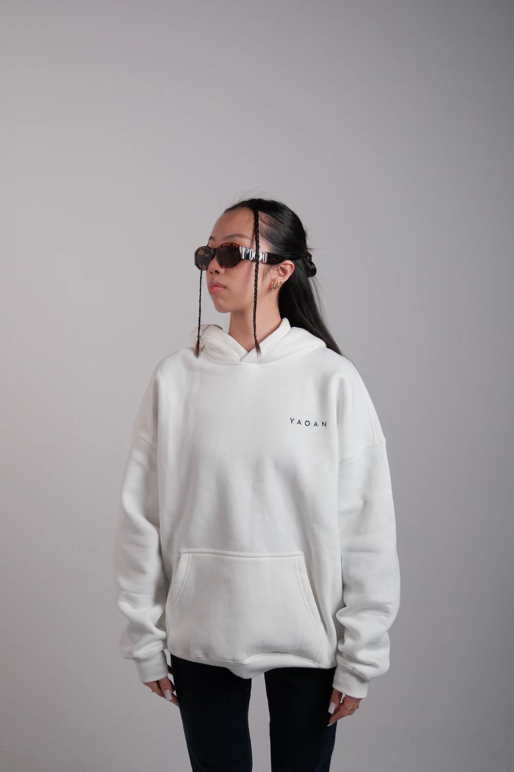A model in a white YAOAN hoodie and sunglasses against a grey studio backdrop.