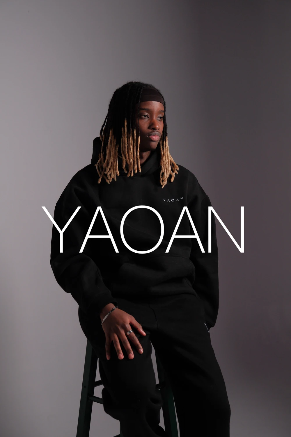 A seated model in a black hoodie with the YAOAN campaign wordmark.