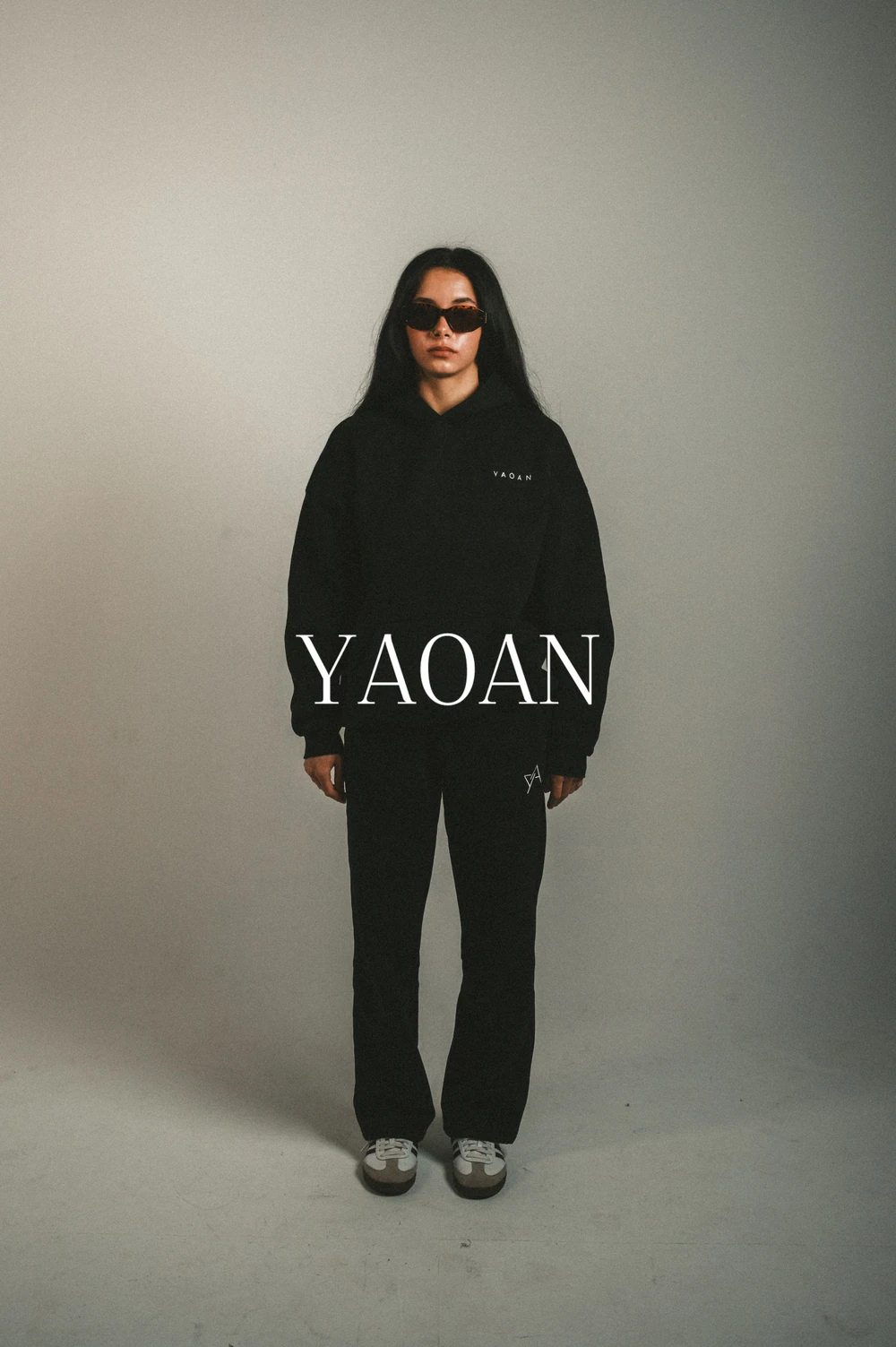 A model in a black hoodie and sunglasses with the YAOAN campaign wordmark.