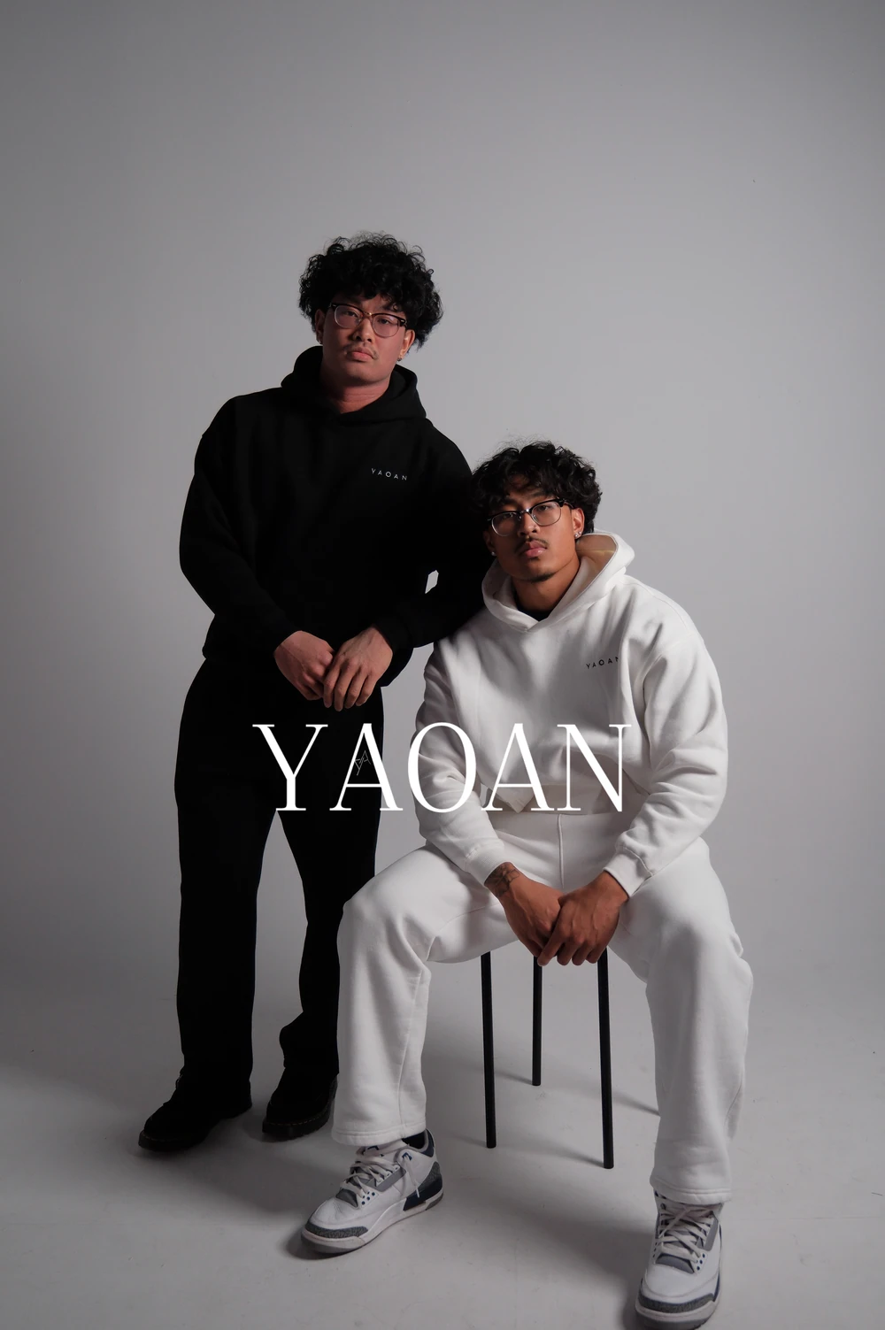 Two models in contrasting black and white hoodies with the YAOAN campaign wordmark.