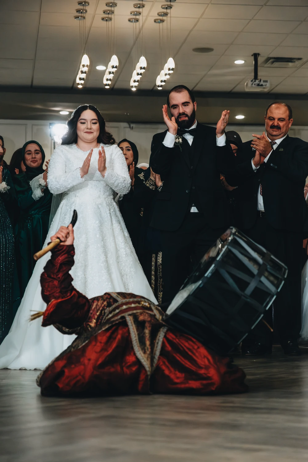 A wedding couple and guests clapping as a drummer performs in the foreground.