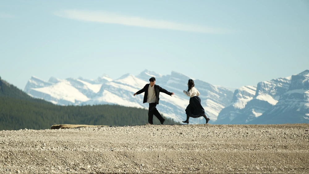 A couple running in an open landscape beneath mountains.