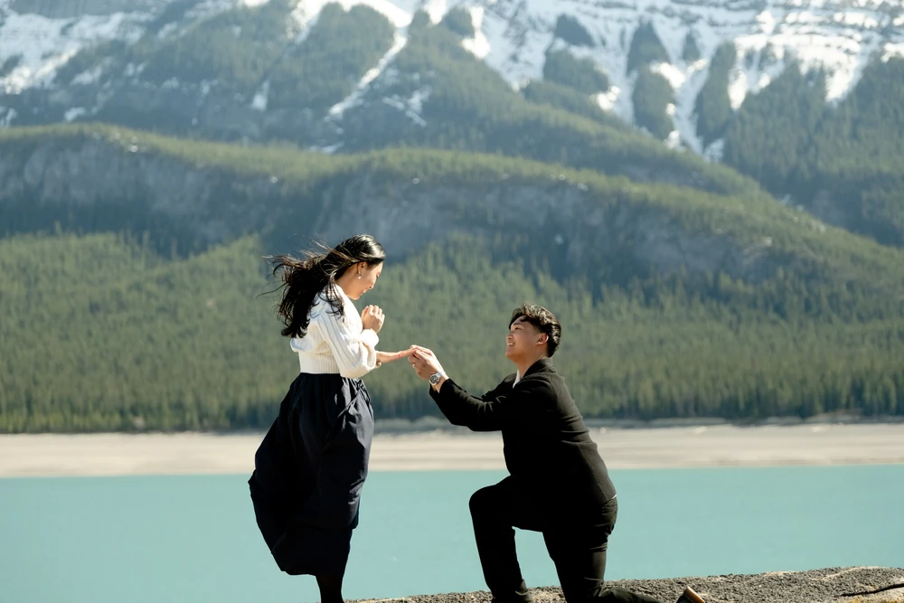 One partner proposing to the other in a mountain setting.