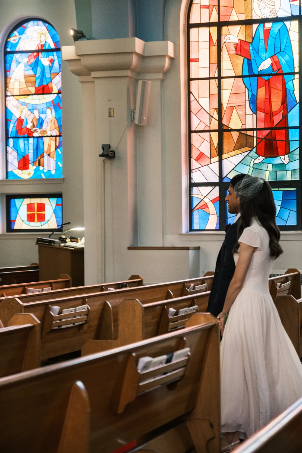 A bride standing beneath stained glass inside a church.