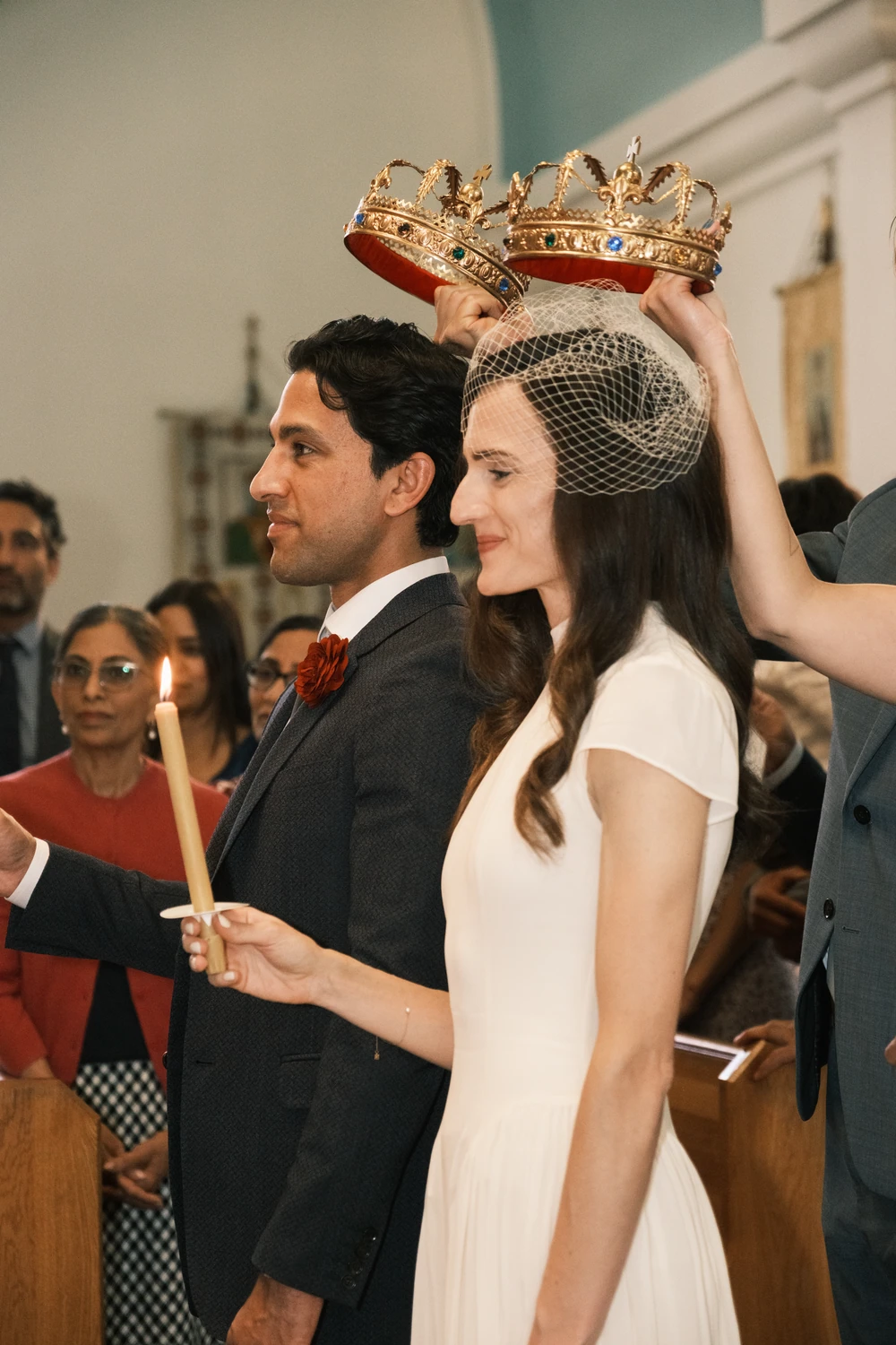 A wedding couple with ceremonial crowns and candles.