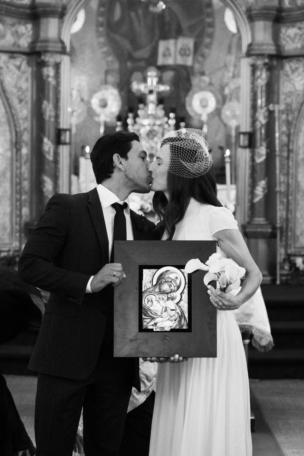 A black-and-white photograph of a couple kissing during their church ceremony.