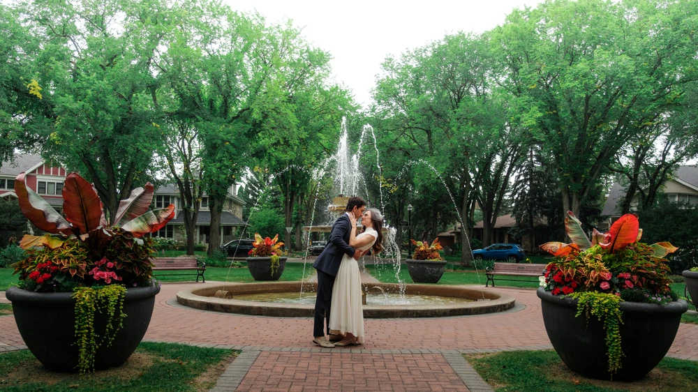 A couple embracing in front of a garden fountain.