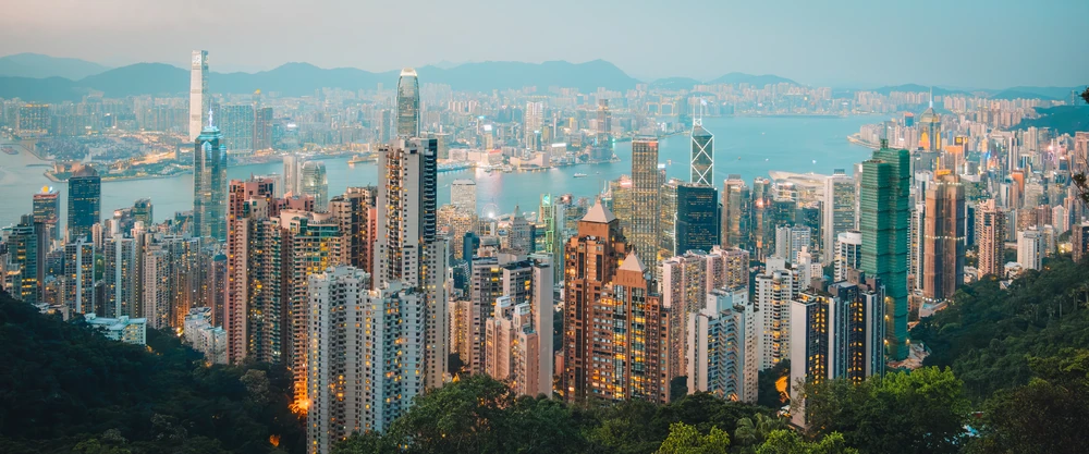 A wide panorama of Hong Kong’s dense skyline and harbour framed by green hills.