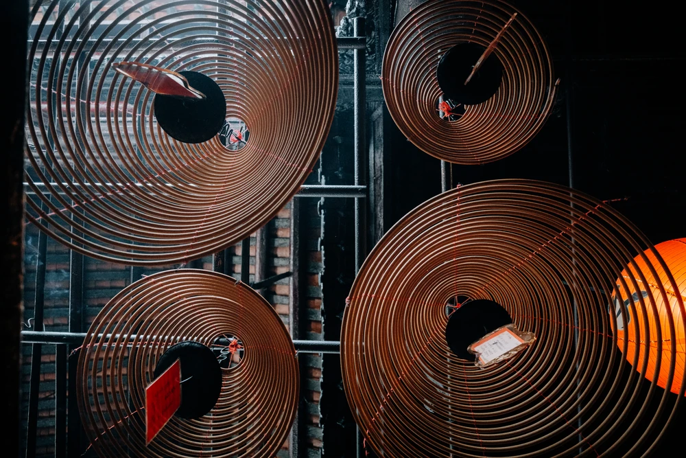 Large circular incense coils and red paper tags against a dark temple ceiling.