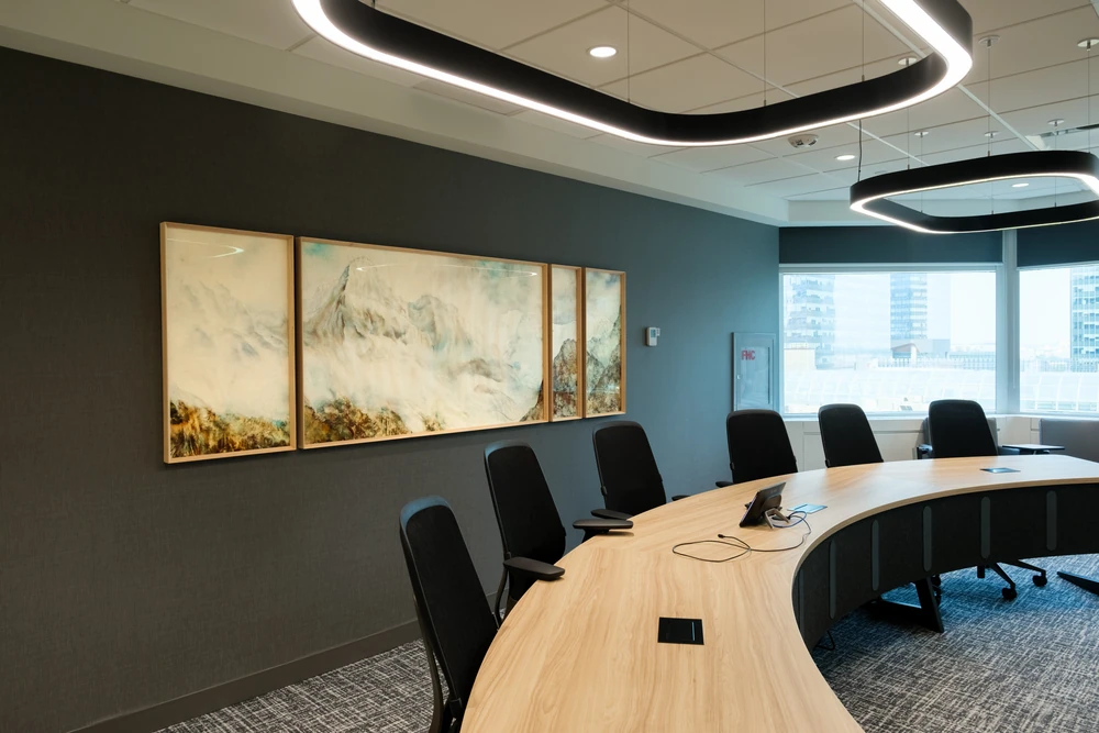 A curved boardroom table, black chairs and a wide artwork beneath sculptural ceiling lights at NBC.