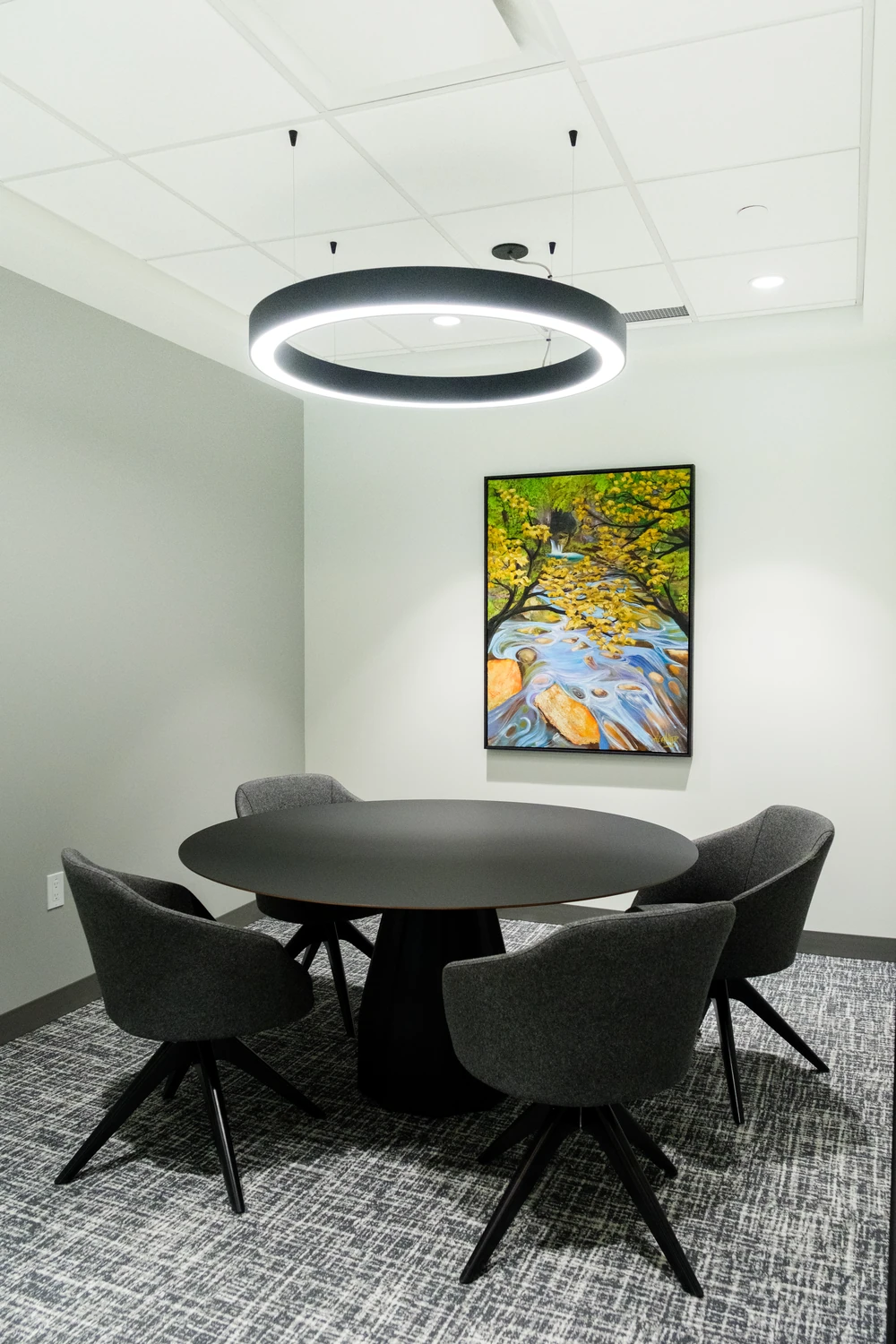 A small meeting room with a round table, circular pendant and colourful artwork at NBC.