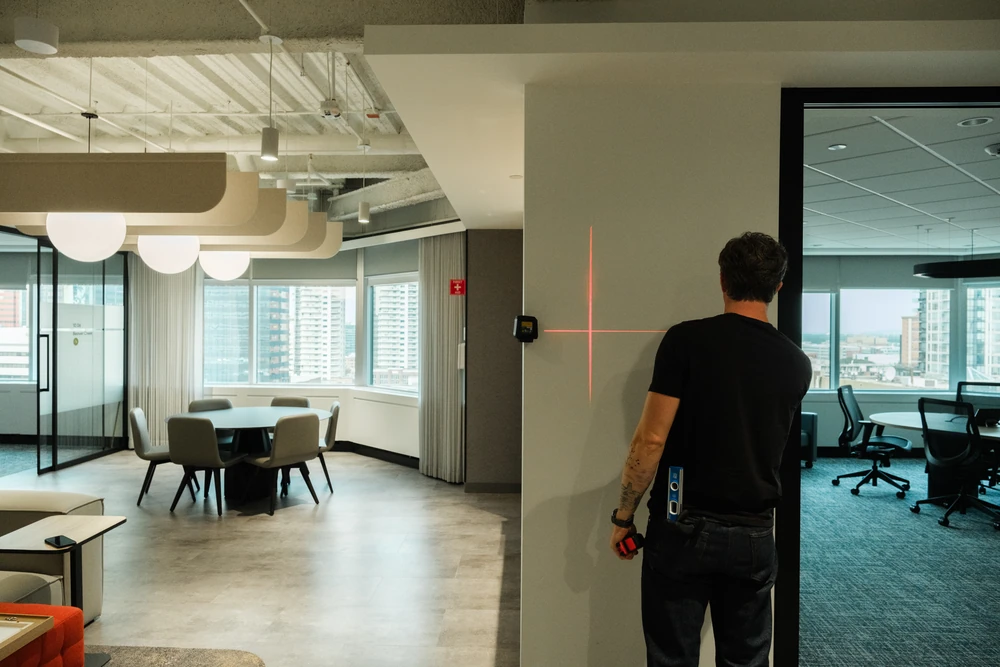 An installer facing red laser alignment lines on a wall within an open NBC office.