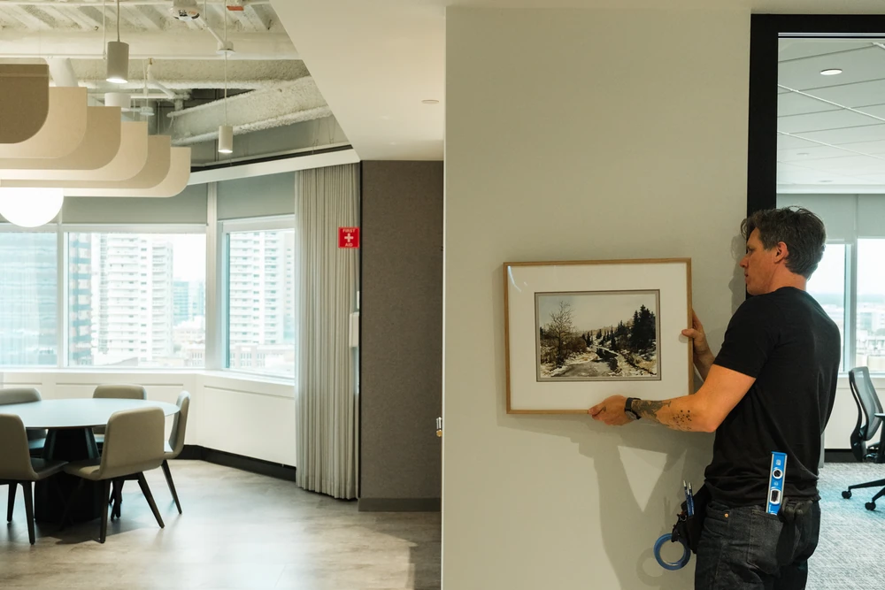 An installer positioning a framed artwork on the office wall at NBC.