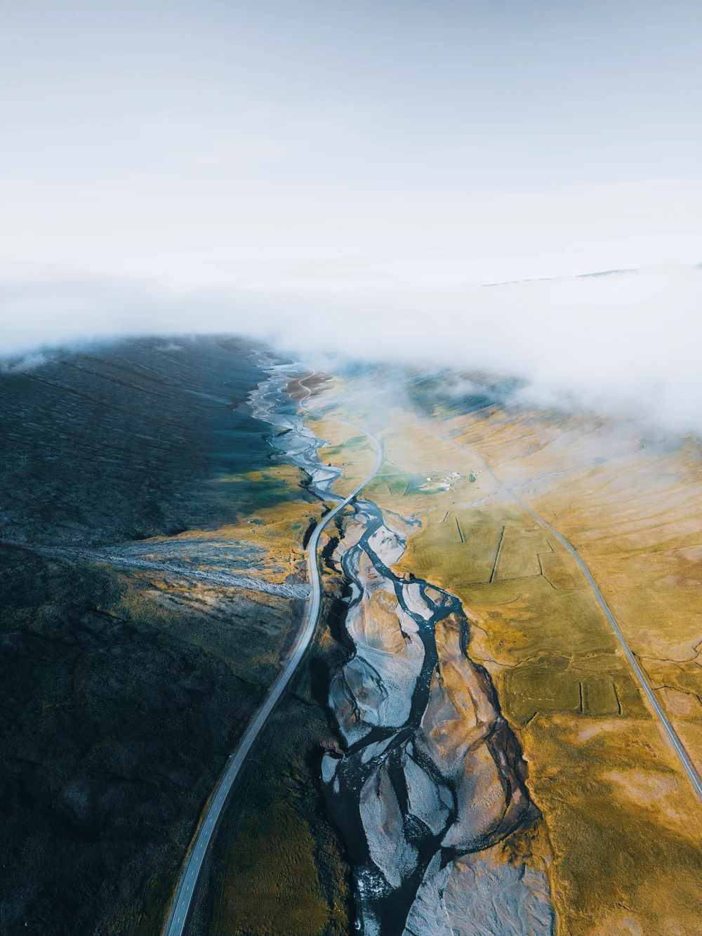 A road and branching river running through a golden Iceland landscape into low cloud.