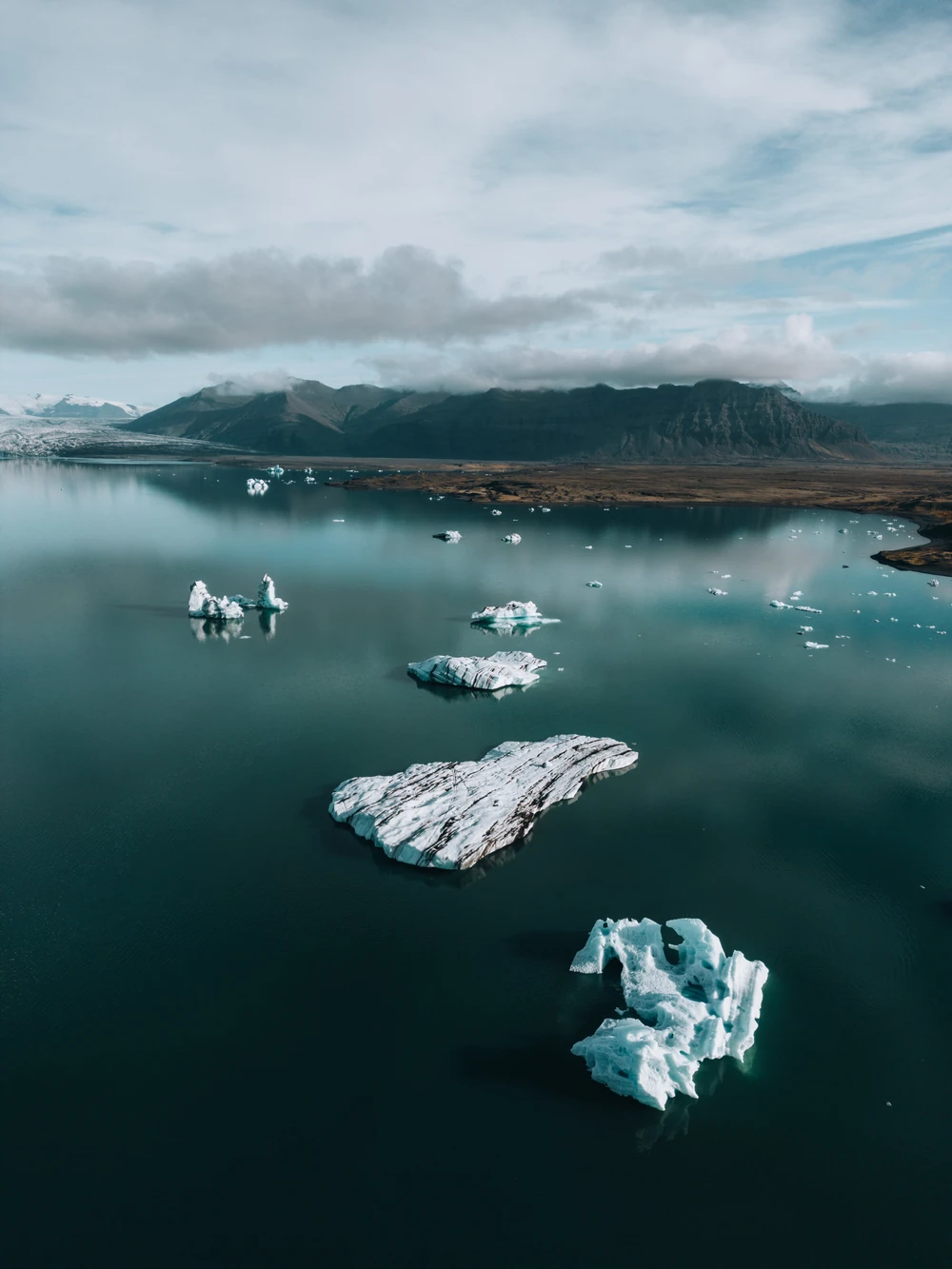 Icebergs floating in a still turquoise lagoon beneath low cloud and dark mountains.