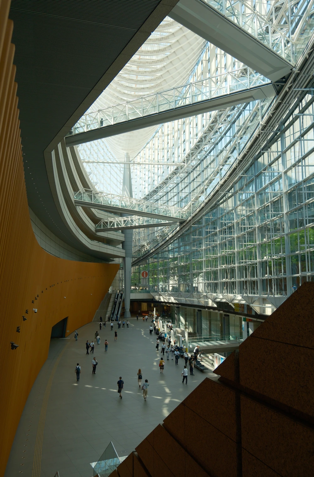 People walking beneath Tokyo International Forum's sweeping glass and steel atrium, seen from above.