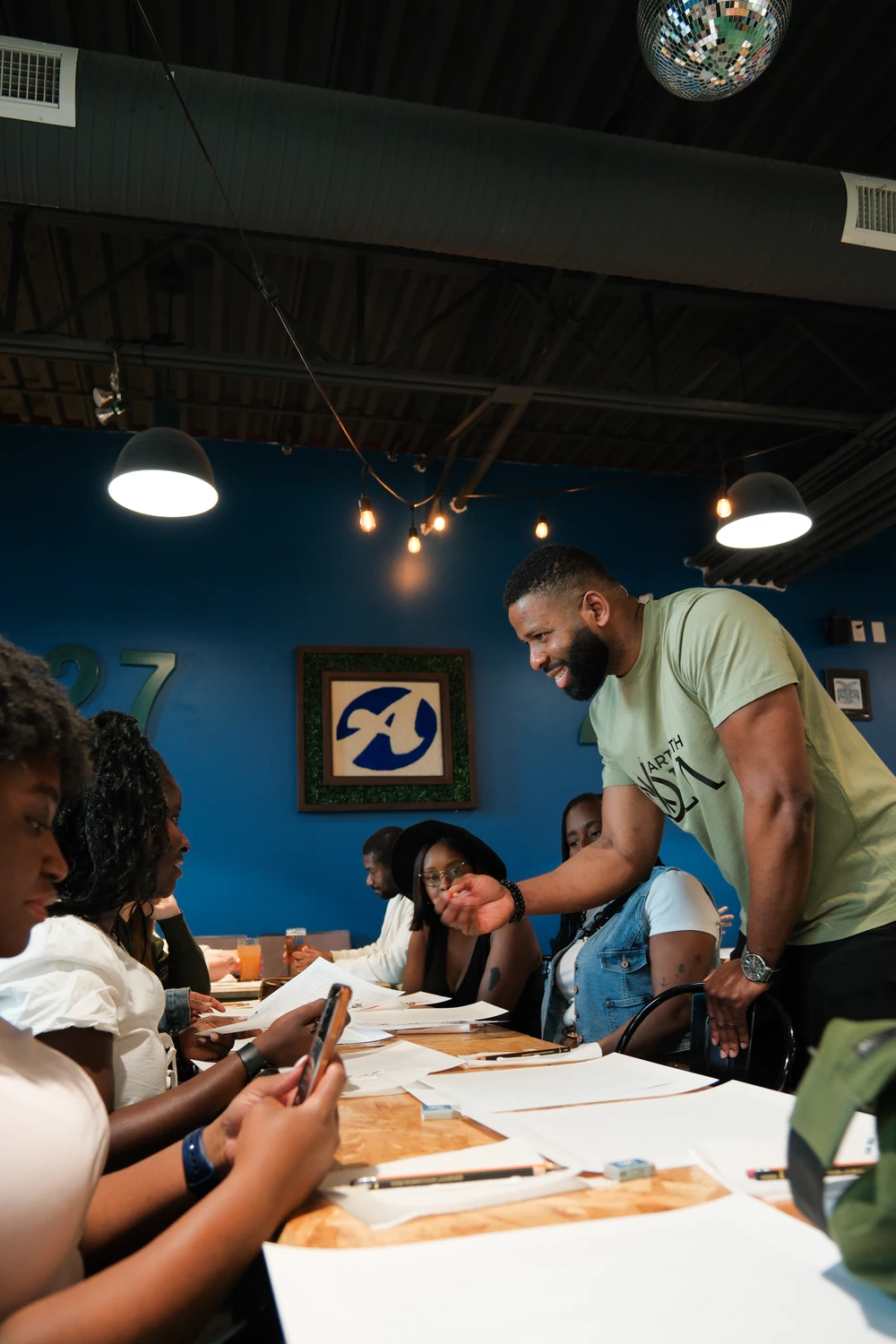 Ola smiling as he leans towards participants and demonstrates with a pencil at a workshop table.