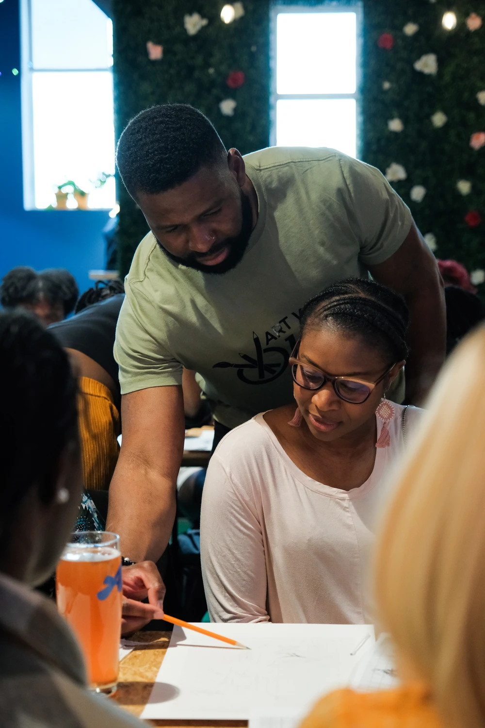 An instructor leaning over to help a participant with a drawing during an Art with Ola session.