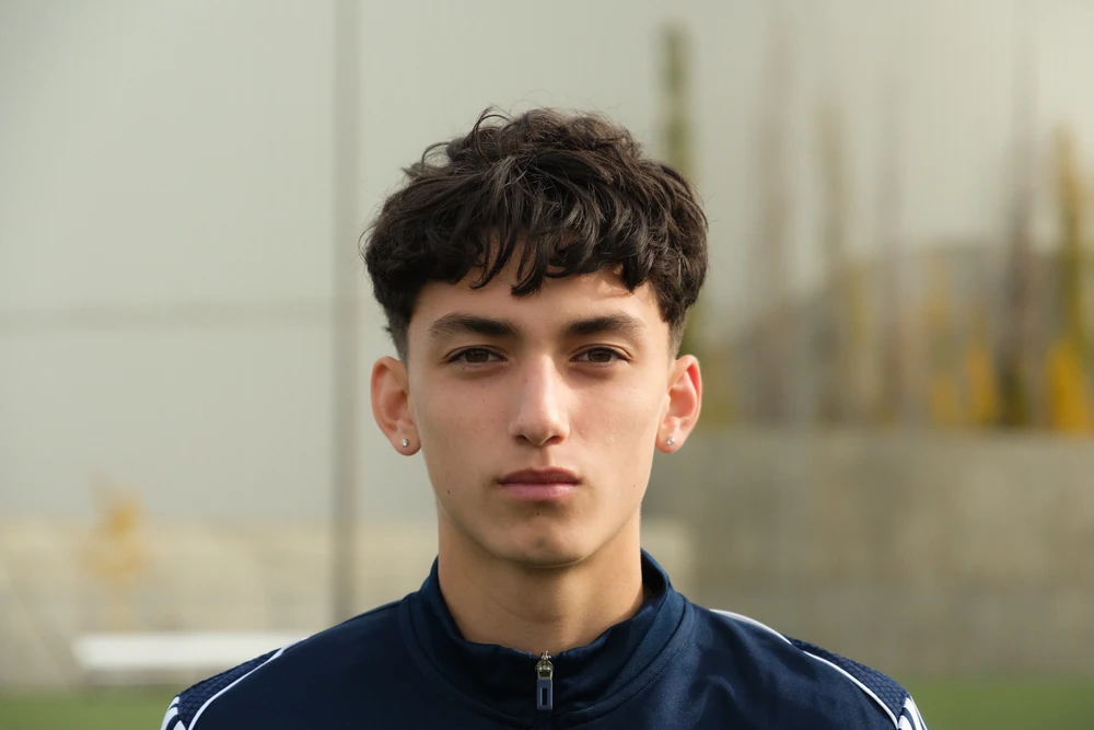 A close portrait of a football player in a navy top, with a softly blurred playing-field background.
