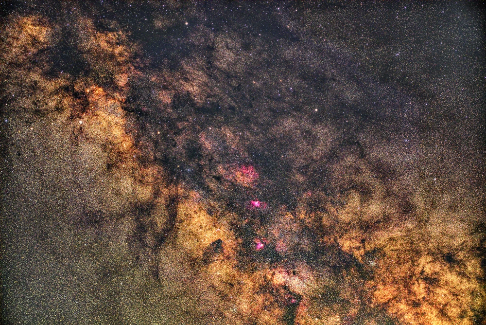 A detailed stacked photograph of the Milky Way, with dense star fields, dark dust lanes and pink nebular regions.